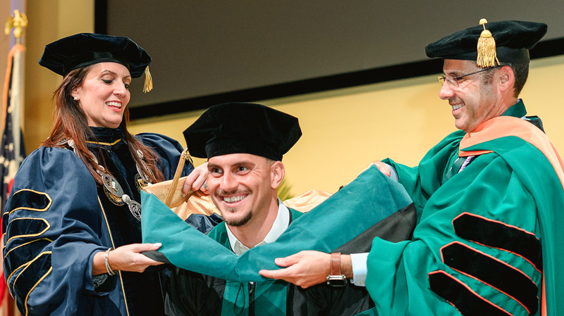 A graduate receives her hood from two faculty members.